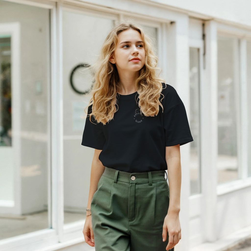 Woman wearing a black t-shirt and green pants standing in front of a glass door.