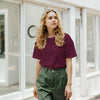 Woman wearing a maroon shirt and green pants standing in front of a glass door.